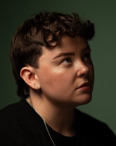 Atmospheric studio portrait of a person with curly hair against a deep green background