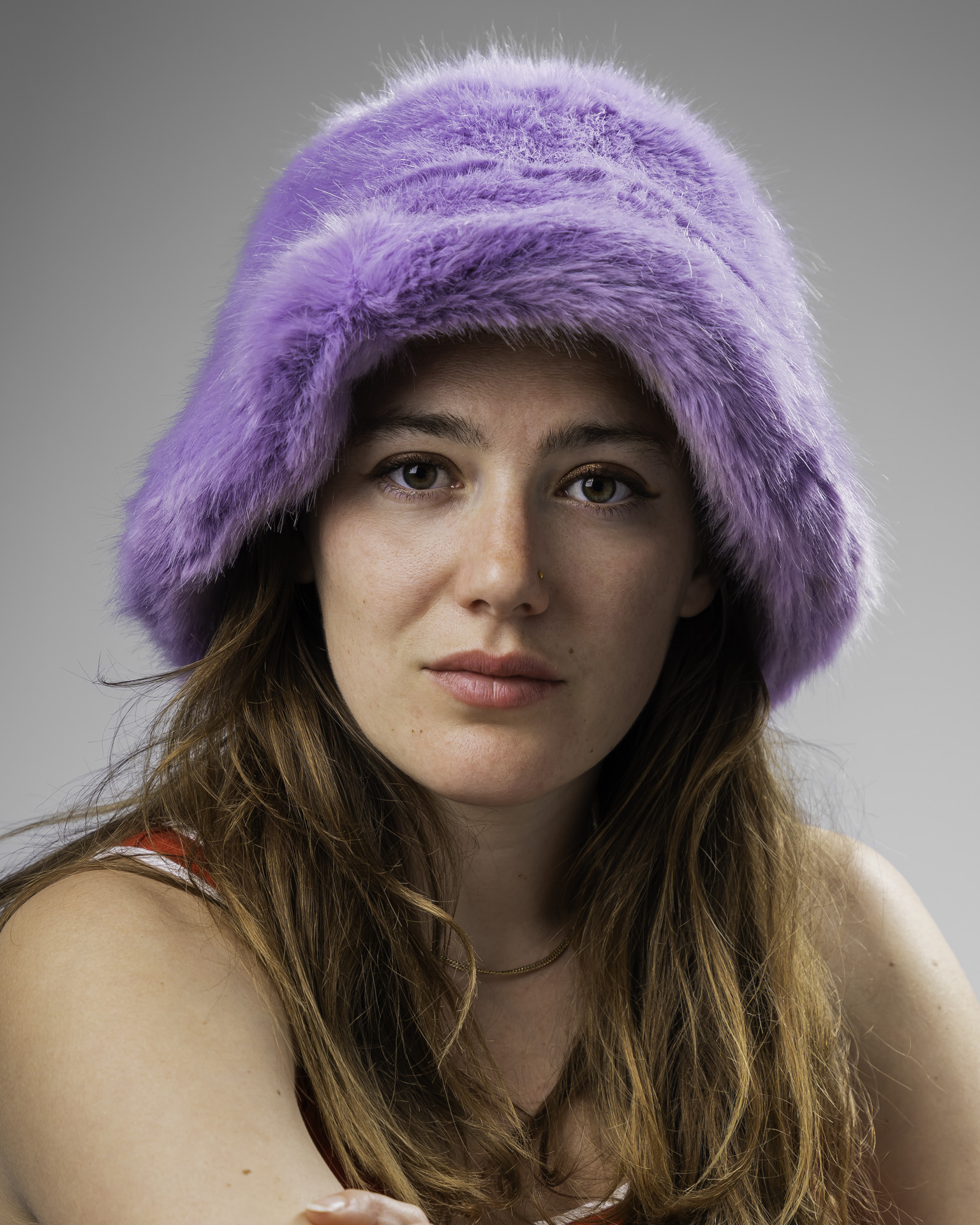 Close-up studio portrait of a woman wearing a fluffy lilac bucket hat against a grey background, shot at Lemon Shark portrait studio London